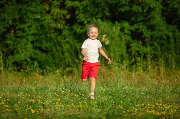 Niño, niño corriendo en la pradera en la luz del sol del verano