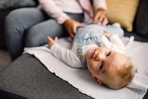 Niño de ojos azules acostado en el sofá y mirando a la cámara mientras está con su madre en casa