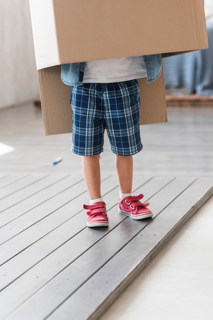 Niño parado debajo de la caja de cartón en el piso de tablones