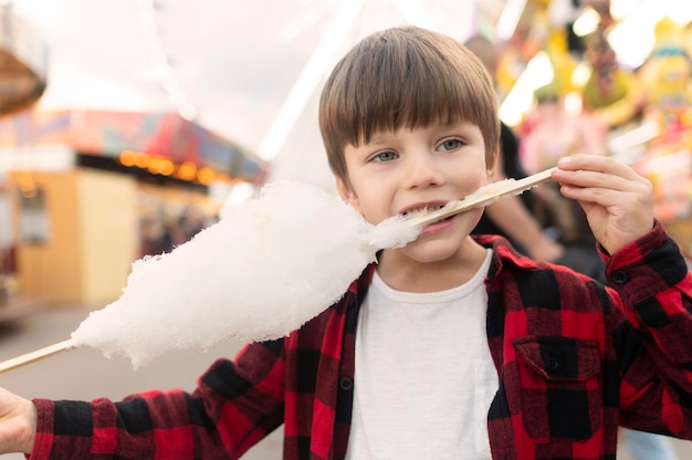 Niño en el parque de diversiones comiendo algodón de azúcar