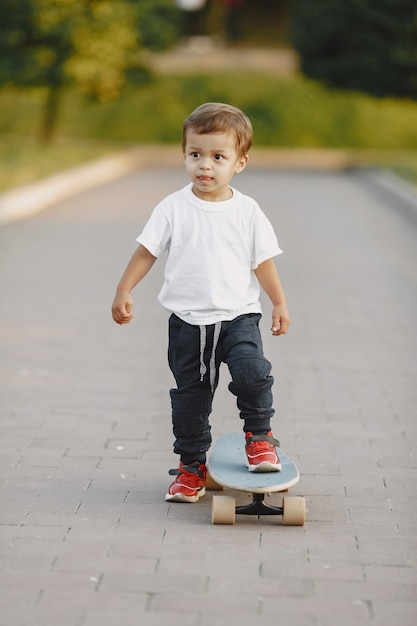 Niño en un parque de verano. Niño con camiseta blanca. Niño con patín.