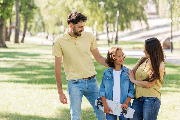 Foto gratuita niño con patineta posando con sus padres en el parque