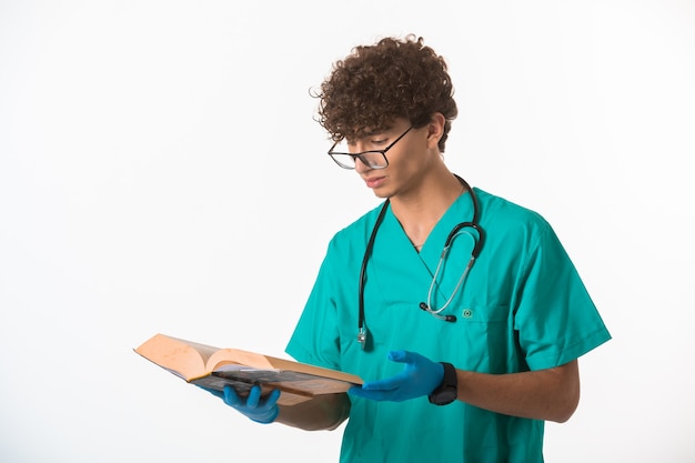 Niño de pelo rizado en uniforme médico y máscaras de mano leyendo un libro viejo