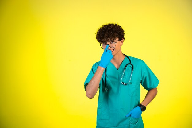 Niño de pelo rizado en uniforme médico y máscaras de mano tocando sus anteojos.