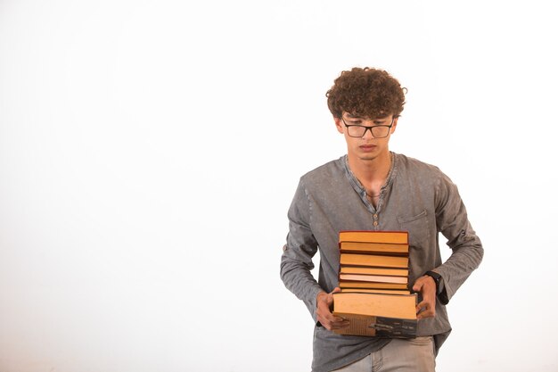 Niño con pelos rizados con gafas ópticas llevando una pila de libros.