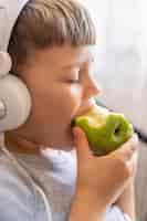 Foto gratuita niño pequeño con auriculares comiendo manzana