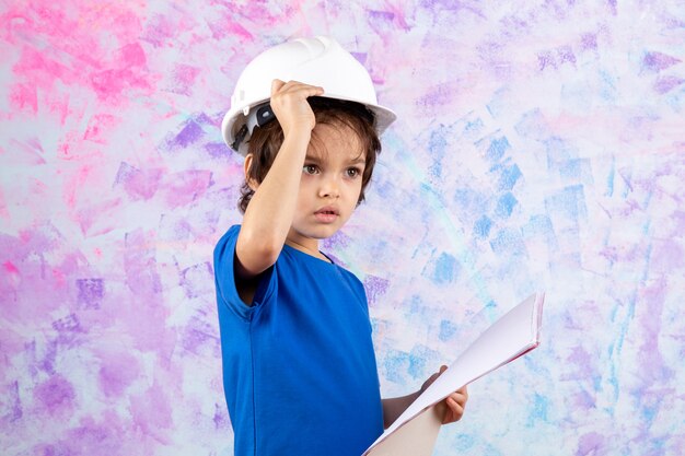 Niño pequeño en casco blanco y camiseta azul con plan de papel en color