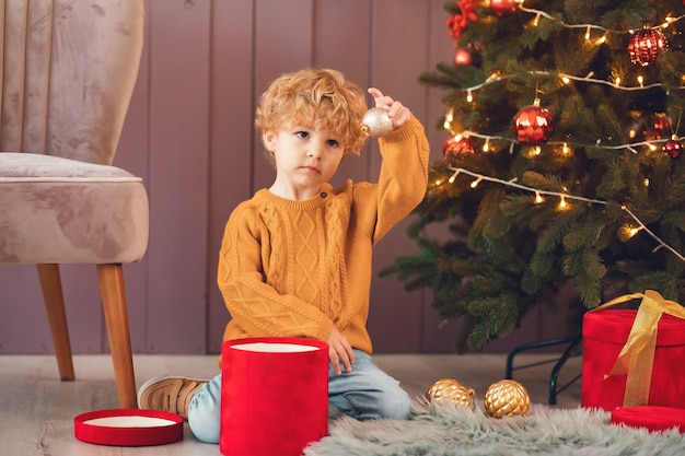 Niño pequeño cerca del árbol de navidad en un suéter marrón