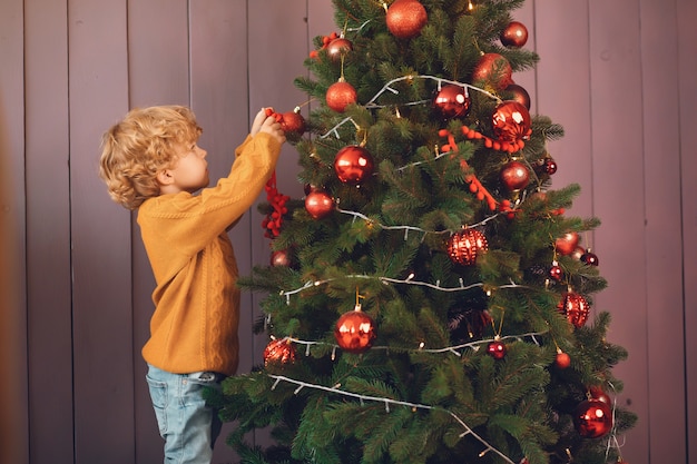 Niño pequeño cerca del árbol de navidad en un suéter marrón