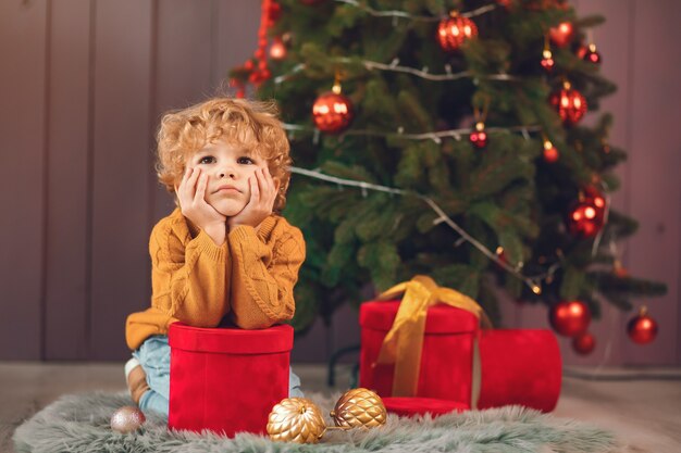 Niño pequeño cerca del árbol de navidad en un suéter marrón