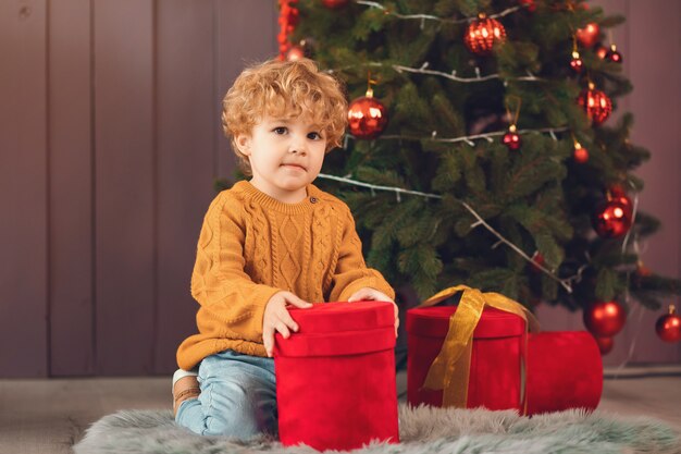 Niño pequeño cerca del árbol de navidad en un suéter marrón