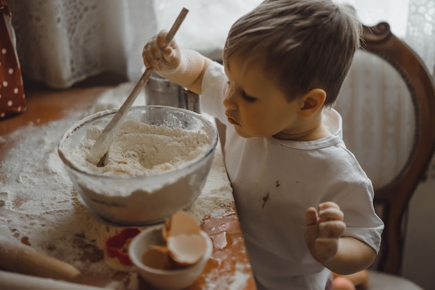 Un niño pequeño en la cocina ayuda a mamá a cocinar. el niño está involucrado en la cocina.