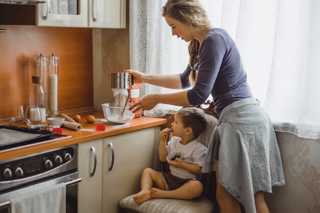 Un niño pequeño en la cocina ayuda a mamá a cocinar. el niño está involucrado en la cocina.