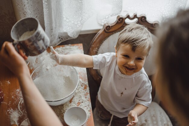 Un niño pequeño en la cocina ayuda a mamá a cocinar. el niño está involucrado en la cocina.