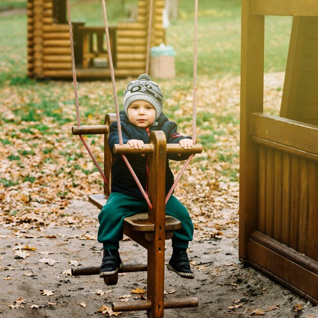 Niño pequeño en columpio en jardín de otoño