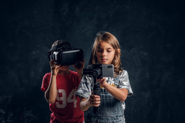 El niño pequeño se divierte usando gafas vr mientras la niña se hace selfie por teléfono móvil.