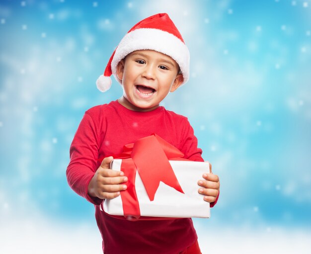 Niño pequeño expresivo con gorro de santa claus y regalo