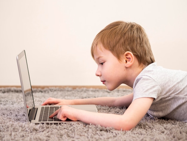 Niño pequeño de lado jugando en su computadora portátil