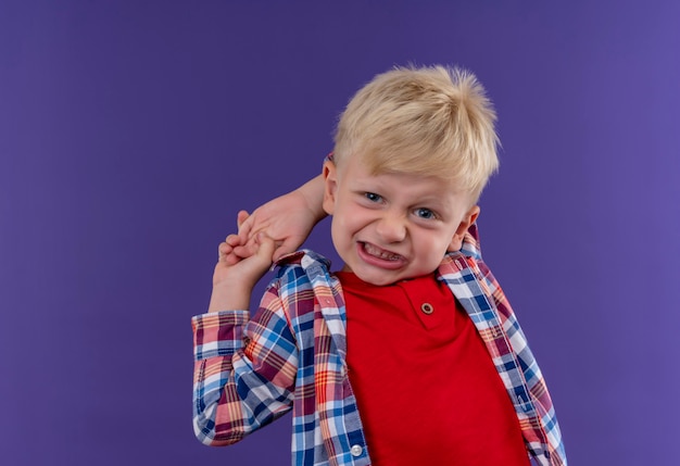 Un niño pequeño lindo agresivo con cabello rubio vistiendo camisa a cuadros mirando