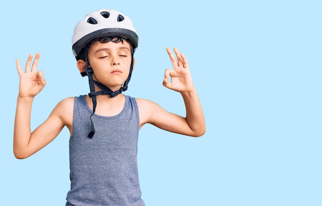 Un niño pequeño y lindo con casco de bicicleta se relaja y sonríe con los ojos cerrados haciendo gestos de meditación con los dedos. concepto de yoga