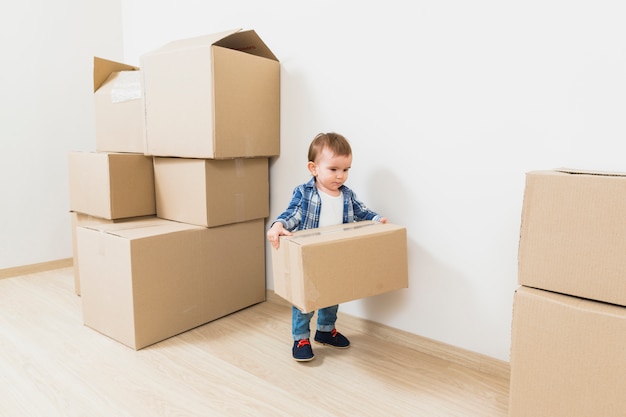 Niño pequeño lindo que lleva las cajas de cartón en el nuevo hogar