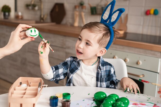Niño pequeño lindo que pinta los huevos de Pascua