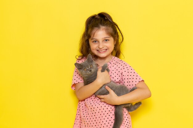 Un niño pequeño lindo de la vista frontal en vestido rosa que sostiene el gatito gris y que sonríe