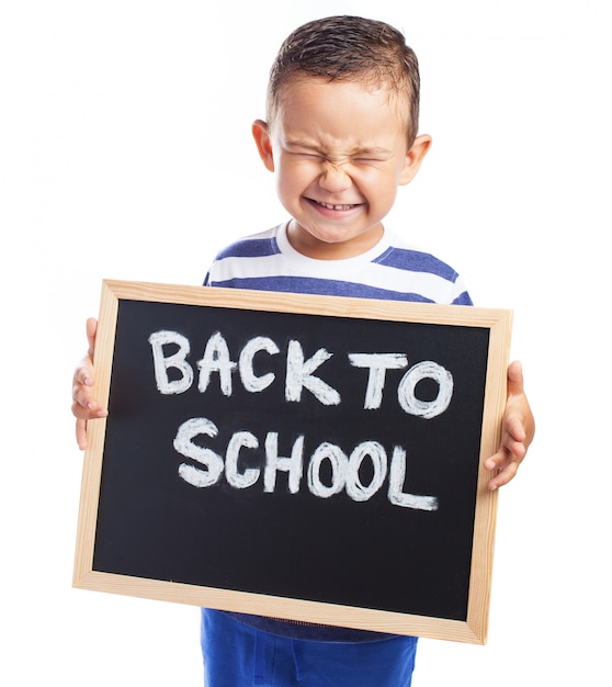 Niño pequeño llorando con una pizarra negra con el mensaje "back to school" 