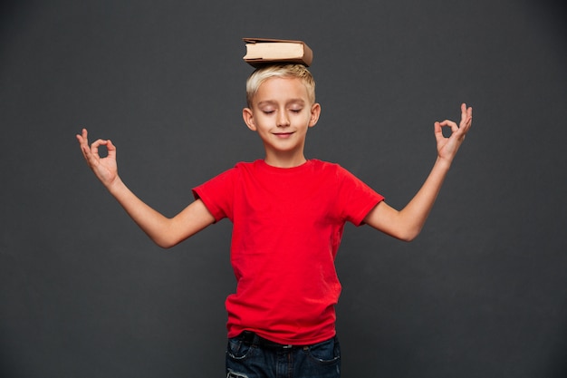 Foto gratuita el niño pequeño medita con el libro en la cabeza.