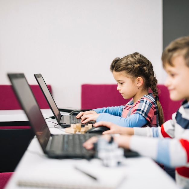 Foto gratuita niño pequeño y niña usando laptop en el aula