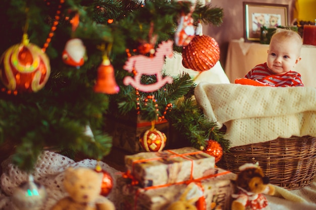 Niño pequeño en pijama despojado se sienta delante de un árbol de Navidad