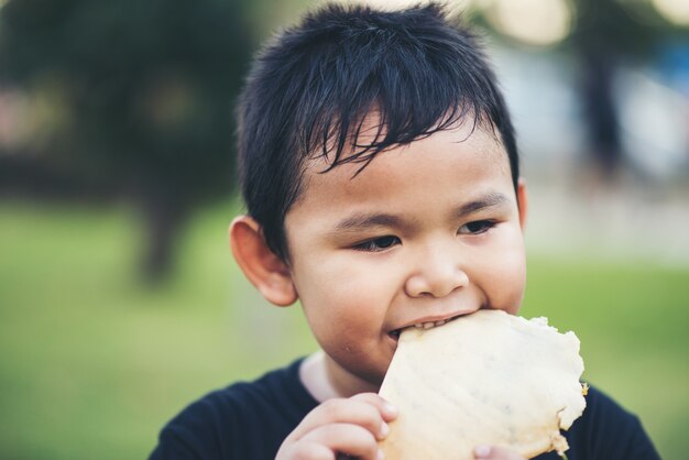 Niño pequeño que come el emparedado del rollo de pan fresco de la comida