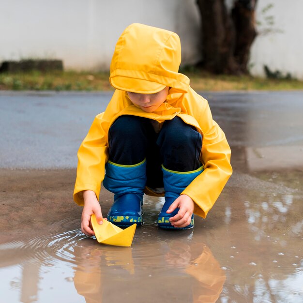 Niño pequeño que juega con un barco de papel amarillo