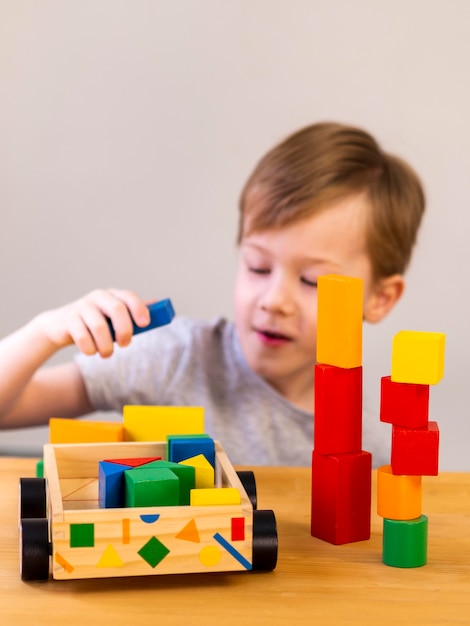 Niño pequeño que juega con los cubos coloridos y el coche de madera