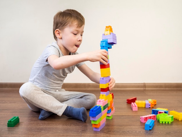 Niño pequeño que juega con el juego colorido del bloque en el piso