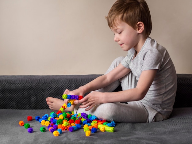 Niño pequeño que juega con el juego colorido en un sofá
