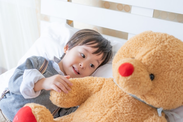 Niño pequeño que juega con el oso de peluche grande en cama