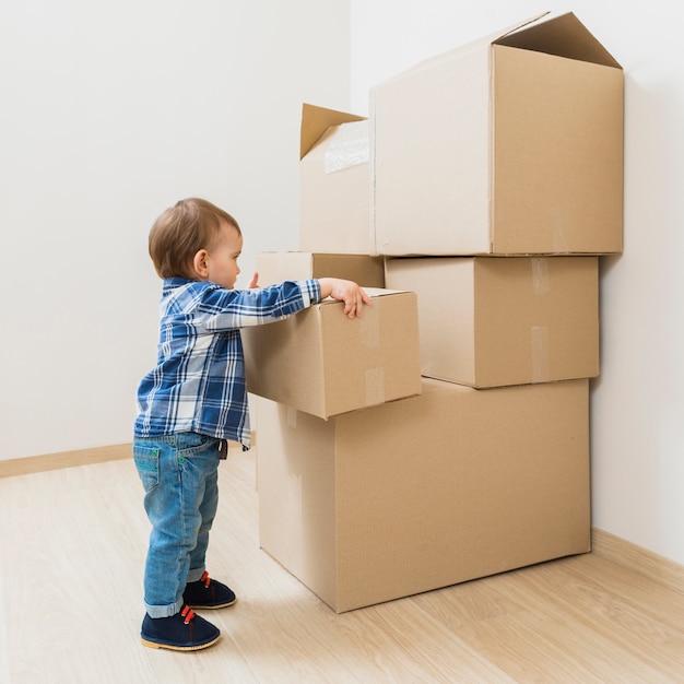 Niño pequeño que lleva la caja de cartón en movimiento en el nuevo hogar