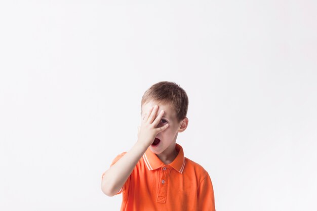 Niño pequeño que mira a través de sus dedos de pie sobre fondo blanco