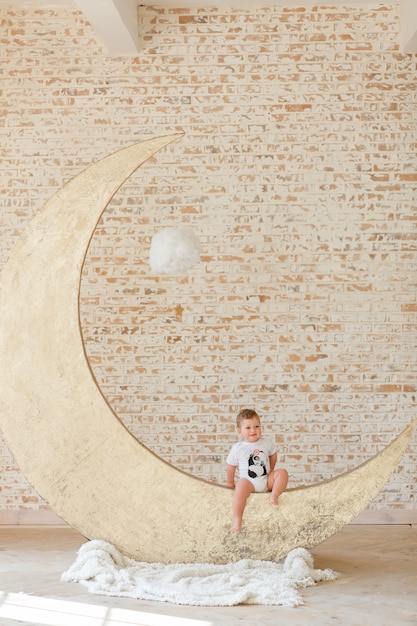 Niño pequeño que presenta en el juguete grande de la luna con el fondo de la pared de ladrillo del desván
