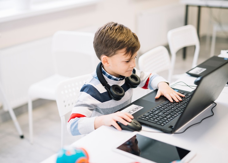 Foto gratuito un niño pequeño que usa la computadora portátil en el escritorio en el aula