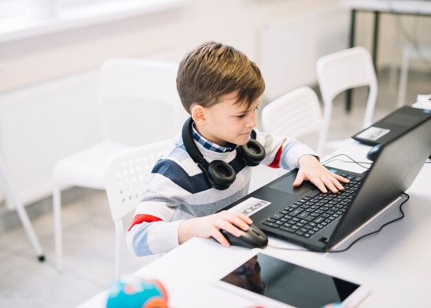 Un niño pequeño que usa la computadora portátil en el escritorio en el aula