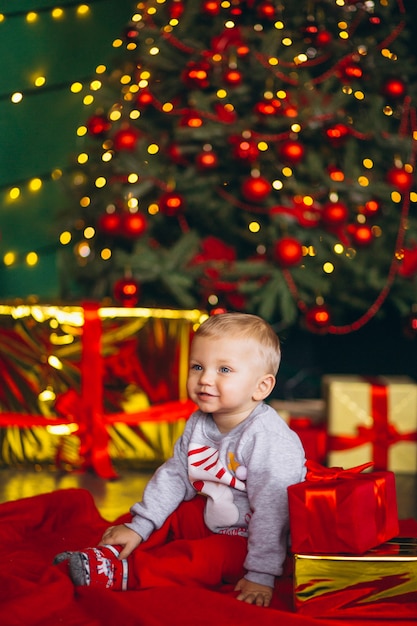 Niño pequeño con regalos navideños por árbol de criostmas.