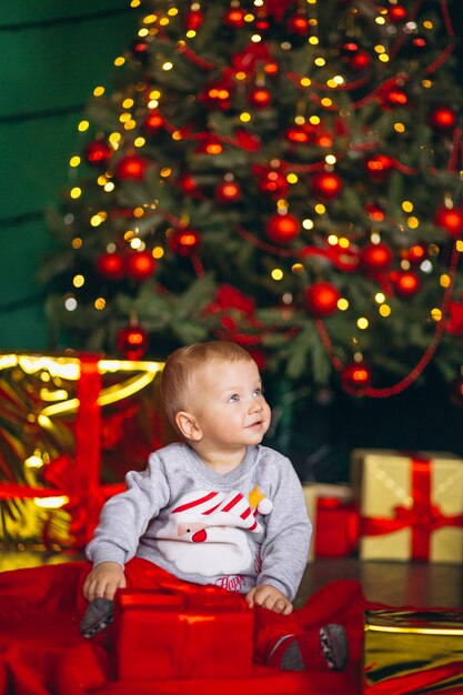 Niño pequeño con regalos navideños por árbol de criostmas.