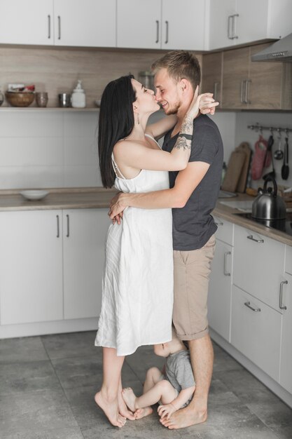 Niño pequeño sentado en los pies de sus padres de pie en la cocina