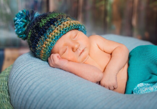 El niño pequeño en sombrero hecho punto duerme en la almohadilla azul grande