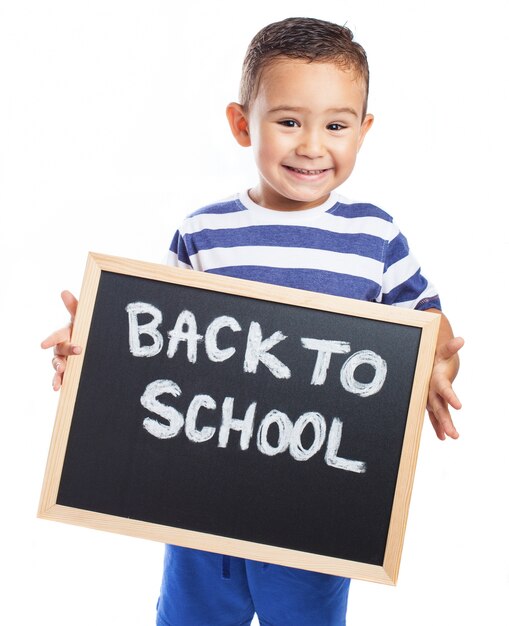 Niño pequeño sonriendo con una pizarra negra con el mensaje "back to school"