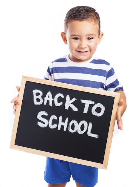 Niño pequeño sonriendo con una pizarra negra con el mensaje "back to school"