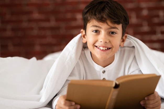 Niño pequeño sonriente que lee en casa