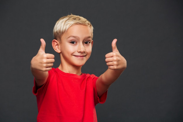 Niño pequeño sonriente que muestra los pulgares para arriba.